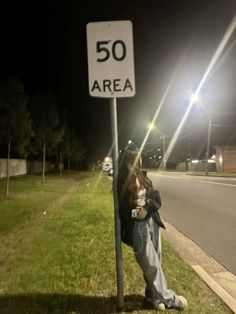 a woman leaning against a street sign on the side of the road at night time