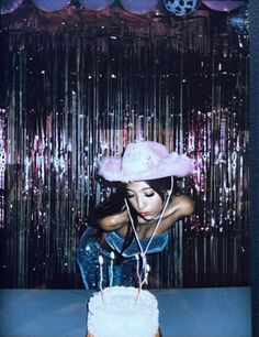 a woman wearing a pink hat sitting in front of a cake with candles on it