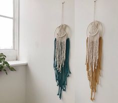 two wall hangings with macrame and tassels on them in front of a window