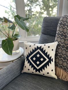 a black and white pillow sitting on top of a gray couch next to a potted plant