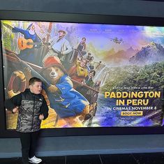 a young boy standing in front of a movie poster at the entrance to paddington's world