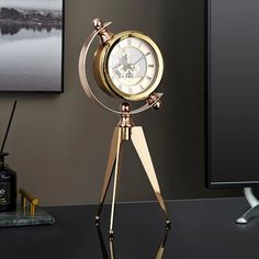 a gold clock on a tripod stand in front of a computer desk with a black background