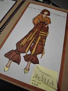 a drawing of a woman's dress and hat on a table next to a notepad