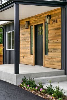 the front porch of a modern home with wood siding and black metal posts on it