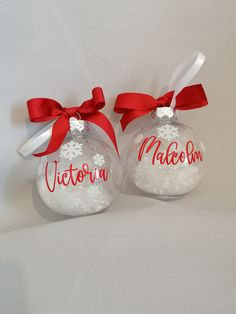 two glass christmas ornaments with red ribbon and name written on one ornament that says victoria