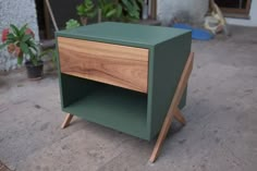 a green wooden side table sitting on top of a cement floor next to a potted plant