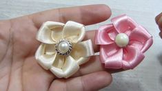 two small flower brooches are being held in someone's hand with pearls on them