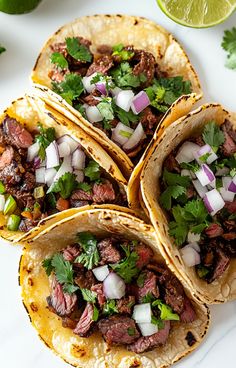 three tacos with meat, onions and cilantro on a white plate next to lime wedges