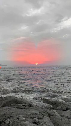 the sun is setting over the ocean with rocks