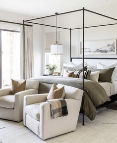 a bedroom with a four poster bed and two couches in front of the window