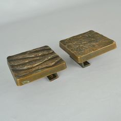 two brass colored square knobs sitting on top of a white surface with no one around them