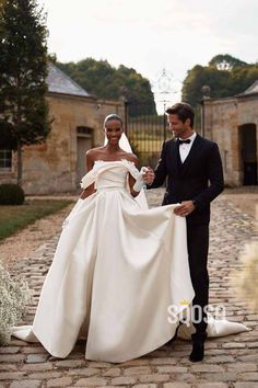 a man and woman in formal wear walking down a cobblestone road