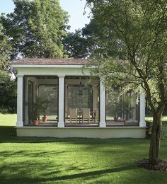 a small white house sitting on top of a lush green field next to a tree