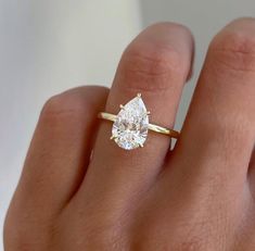 a woman's hand with a yellow gold ring and a pear shaped diamond