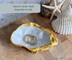 two wedding rings sitting in an oyster shell on a cutting board next to seashells