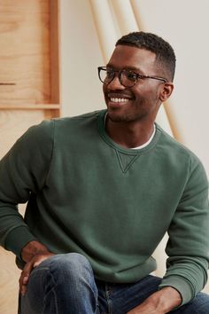 a man sitting on the floor wearing glasses and a green sweater smiles at the camera