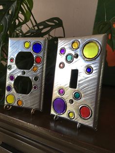 two decorative metal switch plates sitting on top of a wooden table