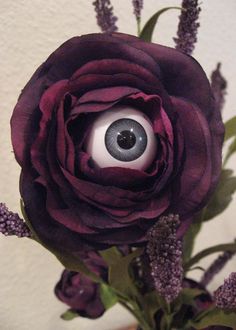 an eyeball is placed in the center of a purple flower, and it appears to be fake