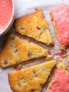 strawberry shortcakes with pink icing on a white surface next to a bowl of fruit