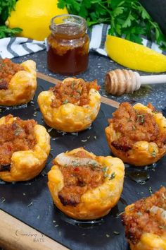 several small muffins with meat and cheese on a tray next to some honey