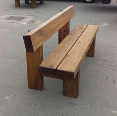 a wooden bench sitting in the middle of a parking lot next to a parked car