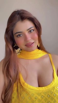 a woman with very large breast wearing a yellow top and gold earrings is posing for the camera