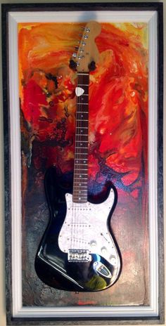 an electric guitar is hanging on the wall in front of a painting with red and orange colors