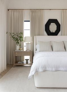 a white bed sitting in a bedroom next to a window with curtains on both sides