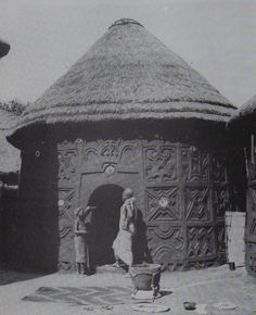 an old black and white photo of some people in front of a hut with thatched roof