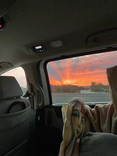 a person sitting in the back seat of a car looking out at an orange sunset