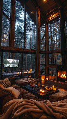 a living room filled with lots of windows next to a fire place in the middle of a forest