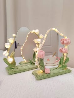 a table topped with two mirrors covered in pink flowers and green leafy decorations next to a white cup