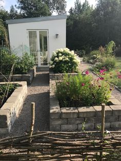 a small white house surrounded by plants and flowers