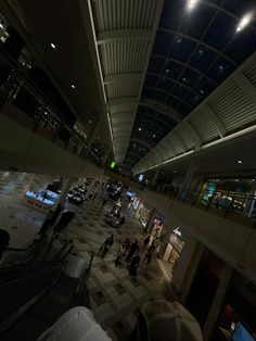 people are walking around in an airport terminal at night, with lights on the ceiling