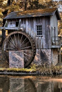 an old water wheel sits next to a small building on the edge of a lake