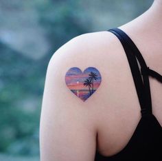 a woman with a heart shaped tattoo on her shoulder and palm tree in the background