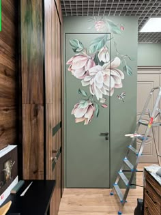 a room with a ladder and painted flowers on the wall next to a green door