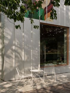 two white chairs sitting on top of a wooden floor next to a building with large windows