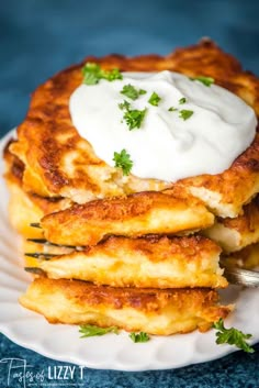 a stack of pancakes with sour cream and parsley on top, sitting on a white plate