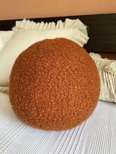 a large brown ball sitting on top of a bed next to two pillows and a pillow