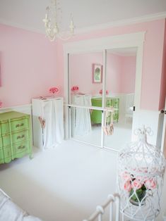 a bedroom with pink walls and green dressers in the corner, white bedding and chandelier