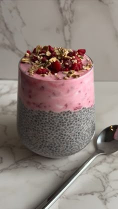 a dessert with fruit and nuts in it on a marble table next to a spoon