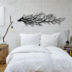 a bed with white sheets and pillows in front of a brick wall that has a tree branch on it