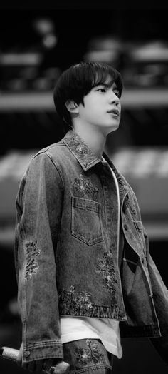 black and white photo of young man in jean jacket looking up at the sky with his hand on his hip