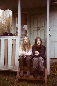 two young women sitting on the porch of a small white house, one with long hair