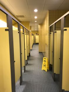 a row of yellow stalls in a hallway with tile flooring and metal posts on either side