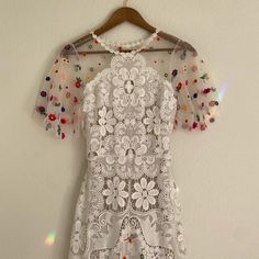 a white dress hanging on a hanger with colorful beads and sequins all over it