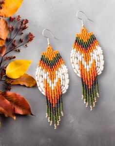 two pairs of beaded earrings sitting on top of a table next to autumn leaves