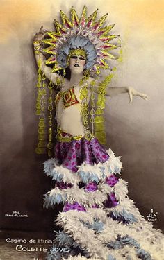 a woman dressed in an elaborate costume with feathers on her head and arms, standing next to a wall