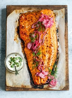 a piece of fish with onions and herbs next to a small bowl of ranch dressing